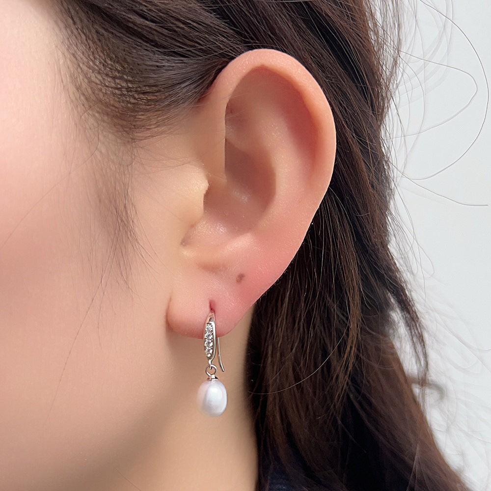 Close-up of pearl drop earring with crystal details worn on ear, showing elegant design