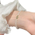 Minimalist bracelet with white pearls and a single light green jade bead, worn against a white textured background