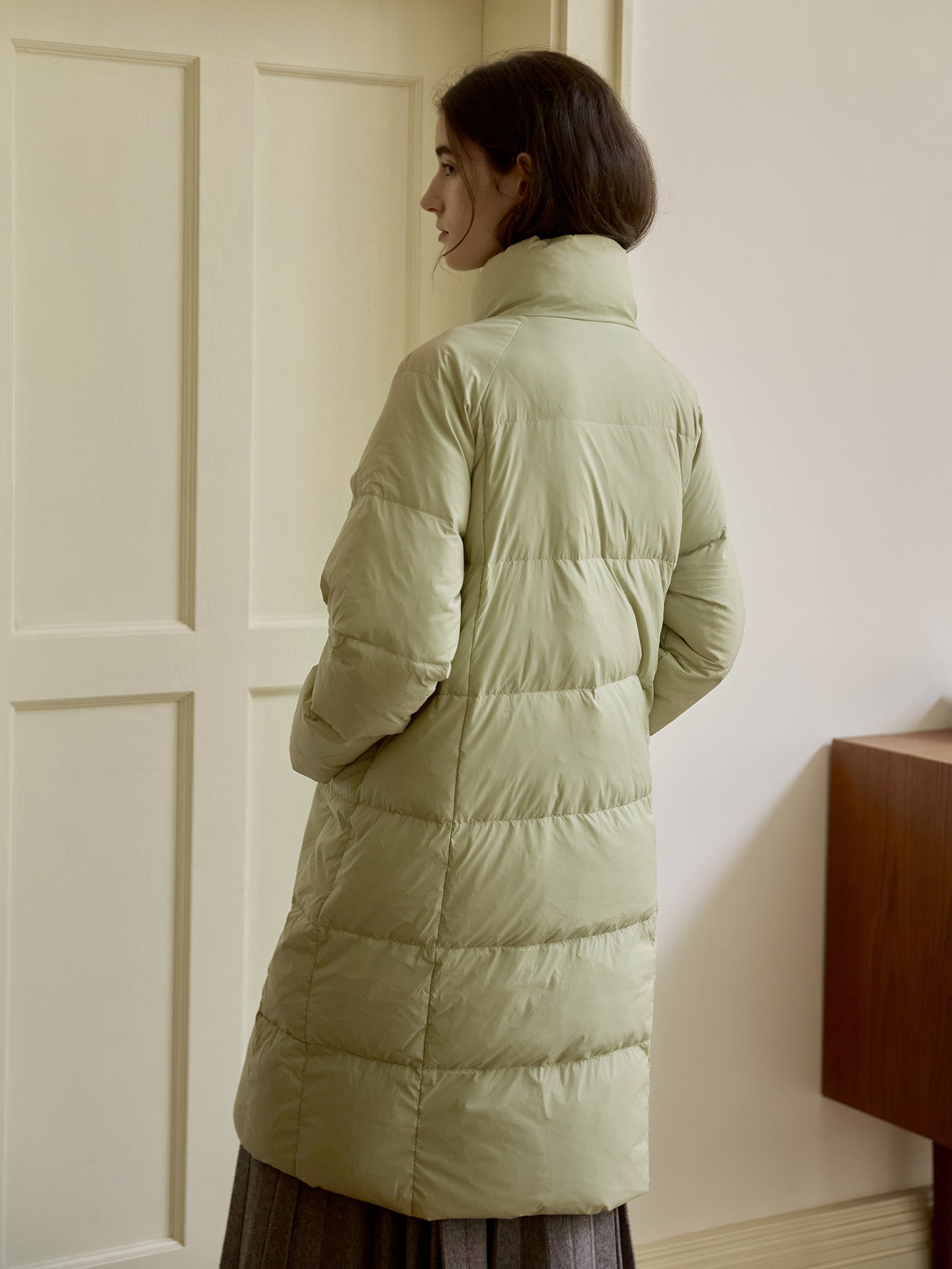Back view of pale sage green puffer coat showing quilted pattern and length, styled with grey skirt