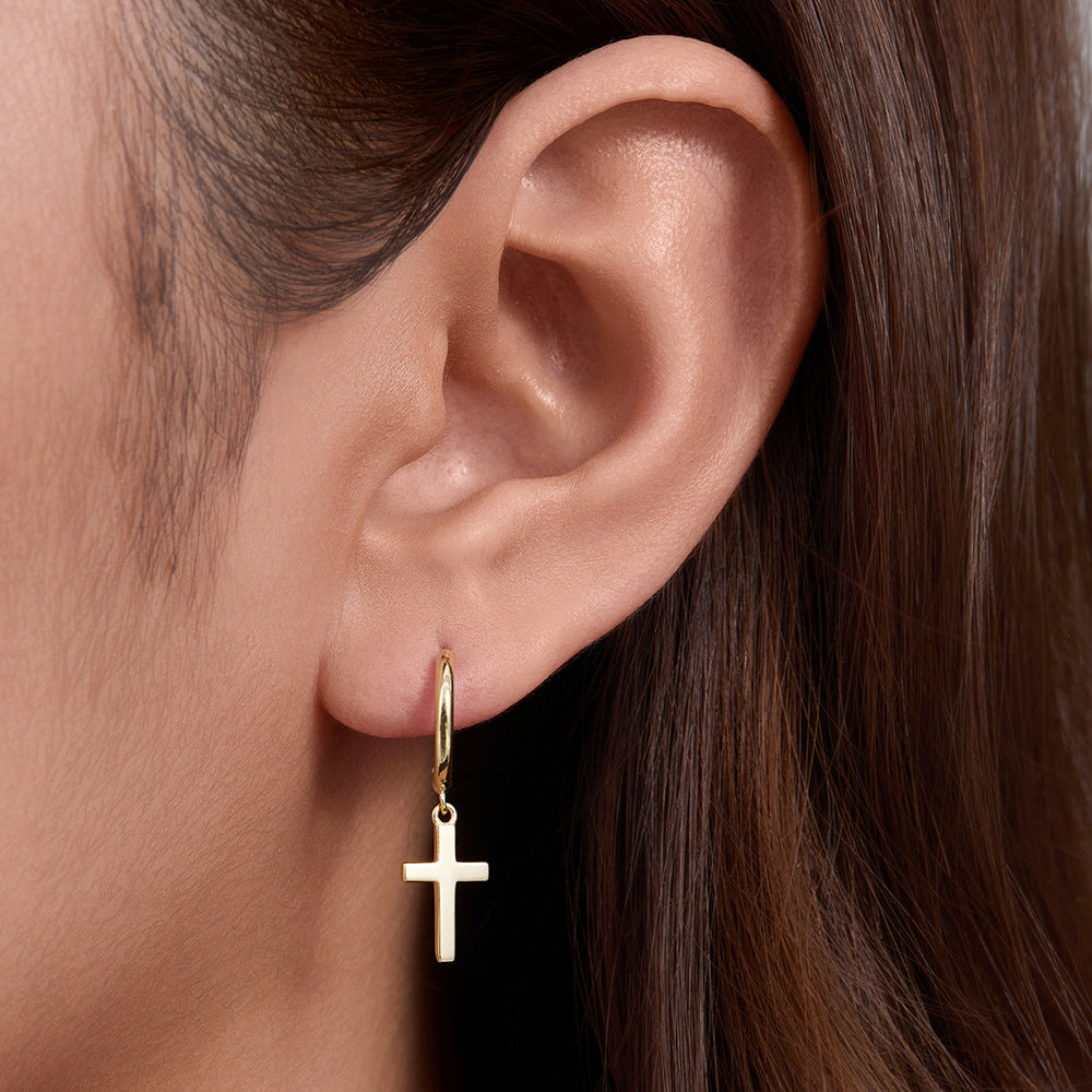 A woman wearing gold cross huggie hoop earring, close-up of ear showing how the small cross pendant hangs from polished hoop
