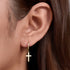 A woman wearing gold cross huggie hoop earring, close-up of ear showing how the small cross pendant hangs from polished hoop