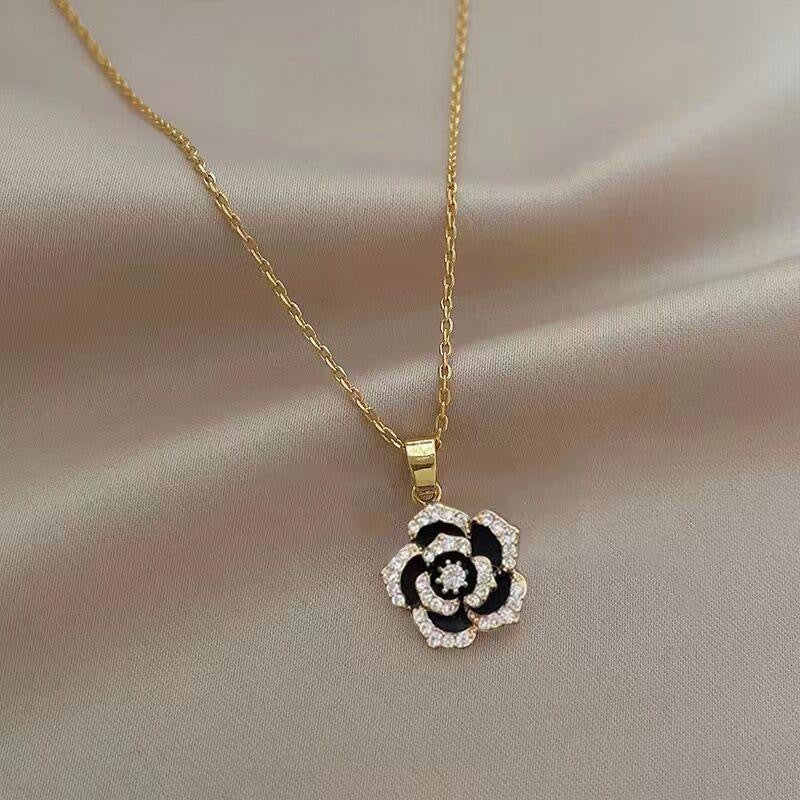 Delicate gold chain necklace with black and crystal flower pendant on silk background
