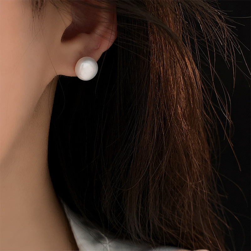 Close-up of white pearl stud earring on ear, shown against dark hair in natural lighting