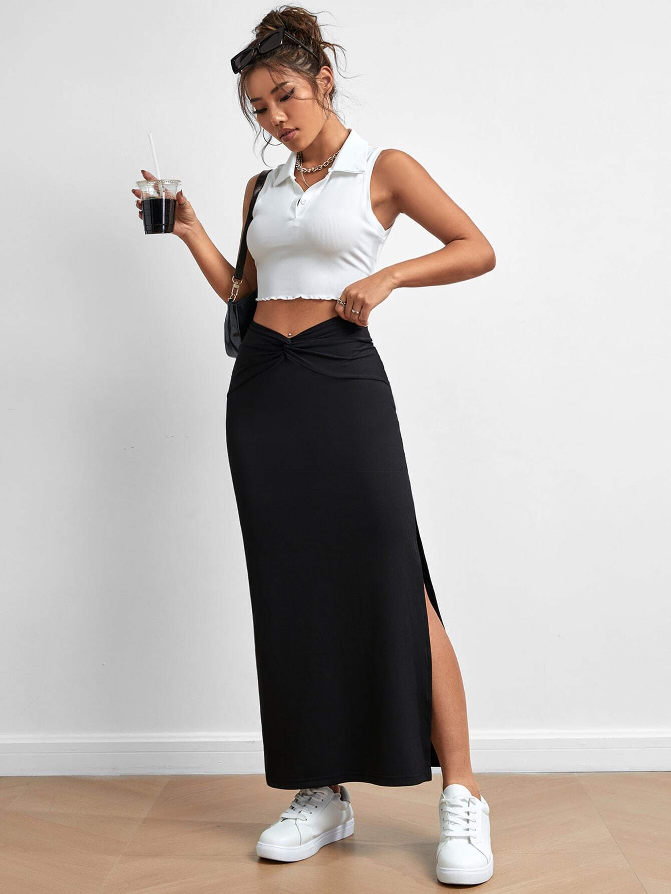 Black long skirt with twisted waistband, worn by a woman in a white crop top, holding a drink, with white sneakers and messy updo