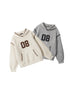 Two varsity-style hoodies with '08' appliqué - one in cream with brown trim and one in heather grey with black trim, featuring contrast whipstitch detailing and kangaroo pockets