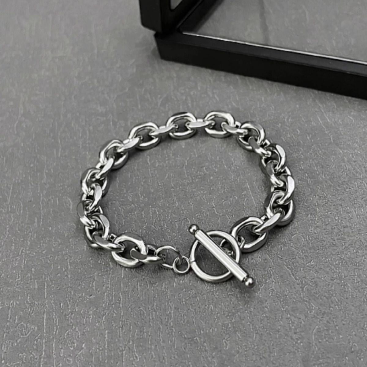 Silver chain bracelet with a toggle clasp resting on a dark surface.