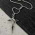 Silver cross pendant necklace with black enamel detail on sturdy box chain arranged on contrasting black and white surfaces