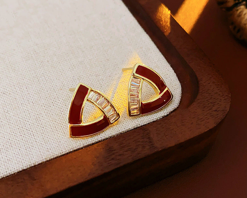 A pair of triangular red enamel and gold stud earrings with baguette-cut crystals is displayed on a fabric-lined jewelry tray