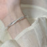 A woman wearing a silver twisted bangle bracelet with crystal accents on her wrist, dressed in white textured fabric