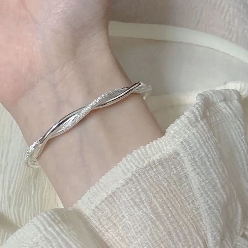 A woman wearing a silver twisted bangle bracelet with crystal accents on her wrist, dressed in white textured fabric