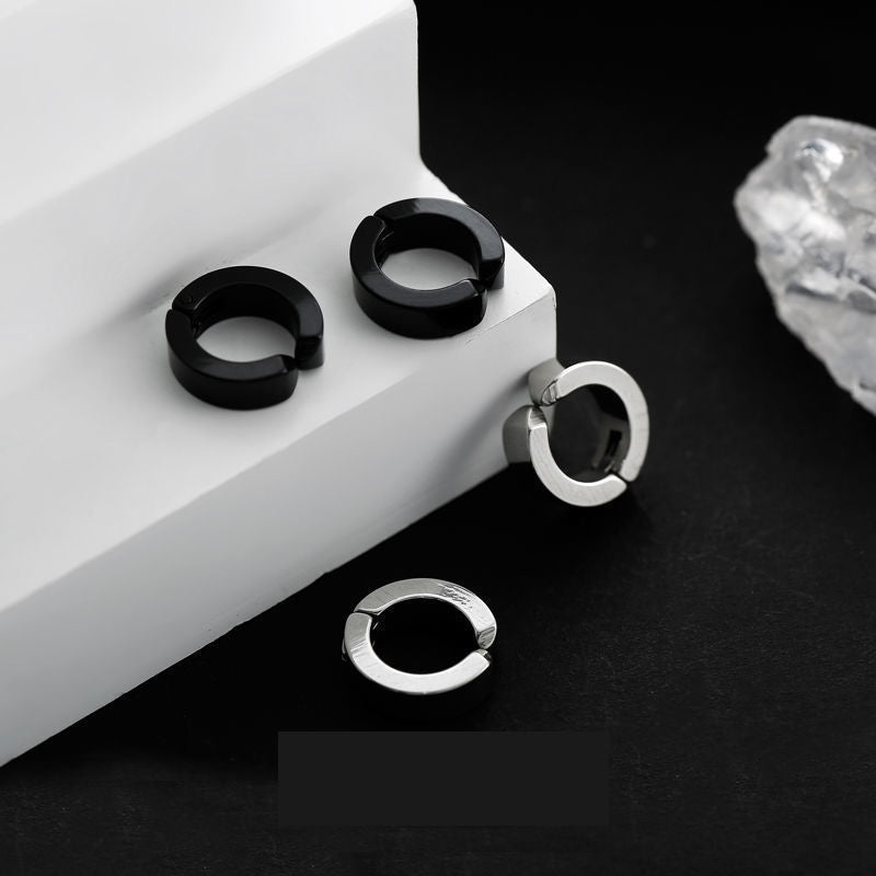 Two pairs of stainless steel huggie earrings in black and silver displayed on white and black contrast surface