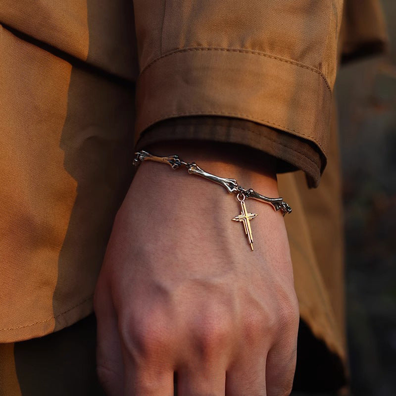  A silver and gold cross bracelet worn with a brown jacket, creating a rugged, vintage-inspired look.