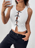  Woman taking a mirror selfie in a stylish white ribbed crop top with black bows and a front cutout, paired with black pants and gold jewelry.
