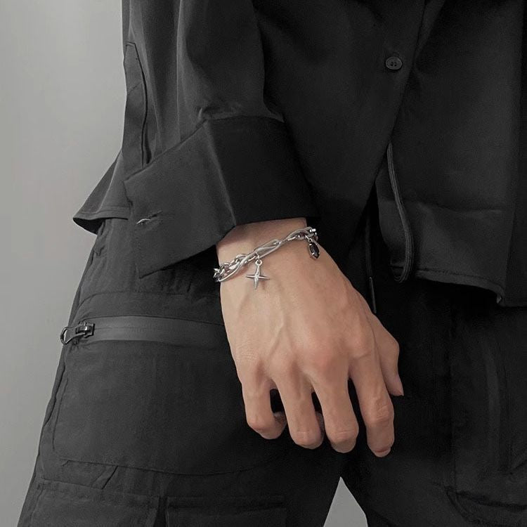 Layered chain bracelet with mixed-link design and cross charm, worn on a wrist with black clothing for a bold statement.
