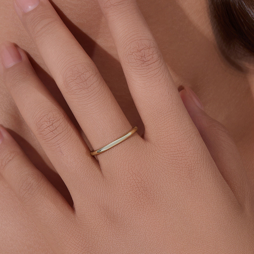 A woman wearing delicate gold band ring on finger against neutral skin tone background