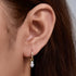 A woman wearing gold huggie hoop earrings with diamond drops on her ear, showcasing how the earrings appear when worn