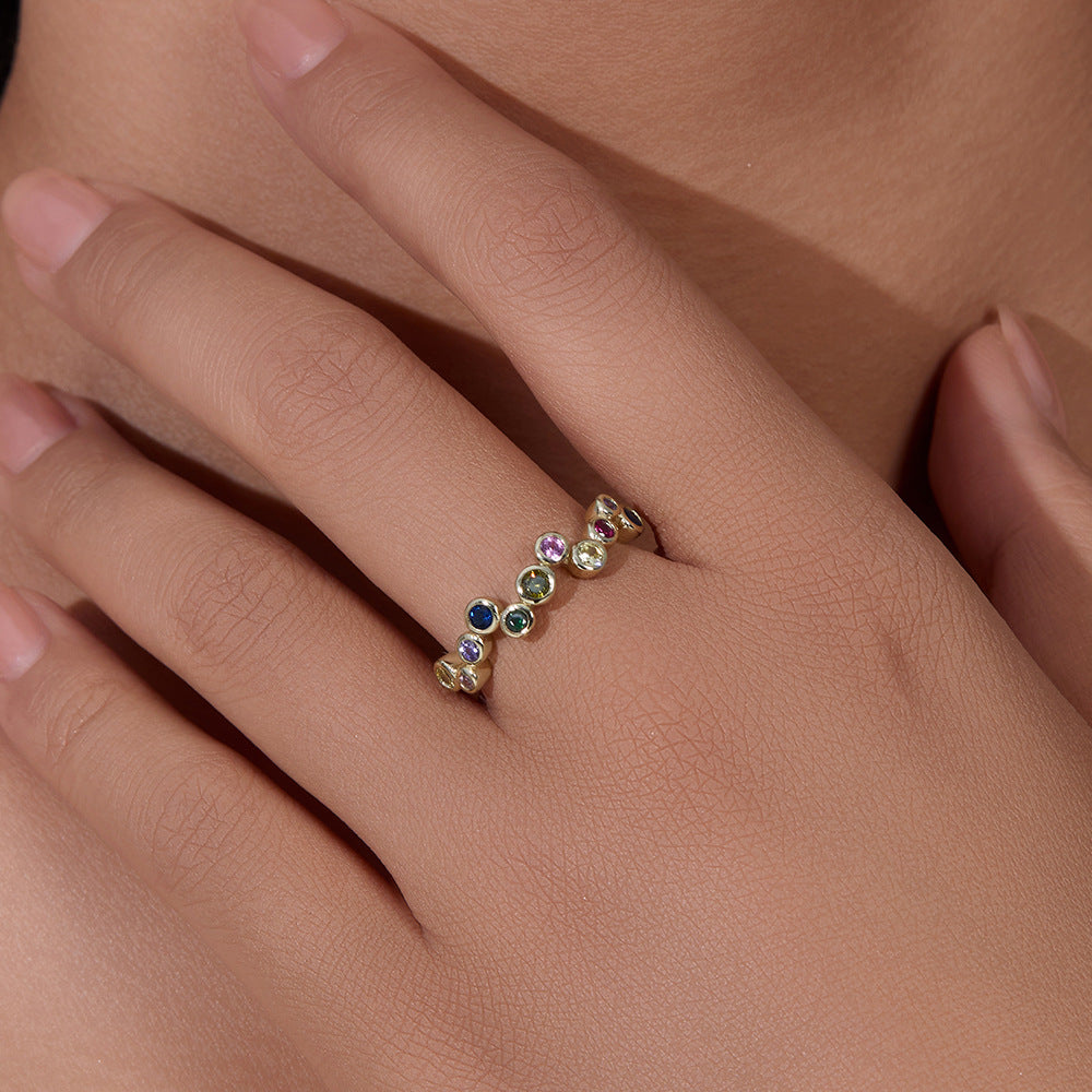 A woman displaying gold bezel-set rainbow gemstone bubble ring on her hand against neutral skin background