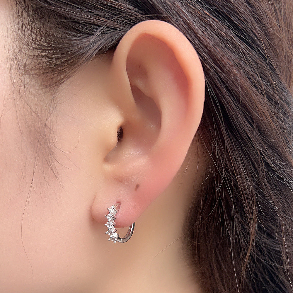 Crystal-adorned silver huggie hoop earring worn on ear, showcasing five-stone design