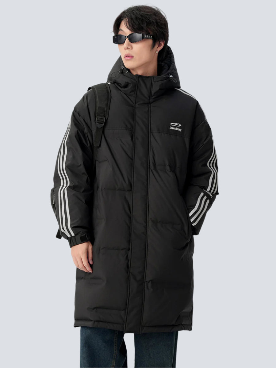 A man is posing at angle wearing black puffer coat with white stripe details against gray background. Features hood, front zip and shoulder backpack strap