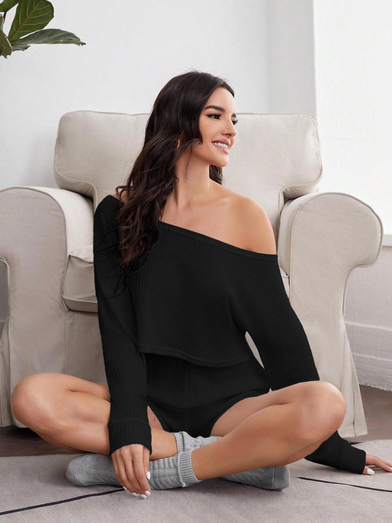 Woman in black knit loungewear set sitting cross-legged on couch, wearing gray socks and smiling
