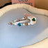 Teardrop-shaped silver hair clip with iridescent gemstones in heart shapes, featuring a pearl accent, displayed on blue fabric.