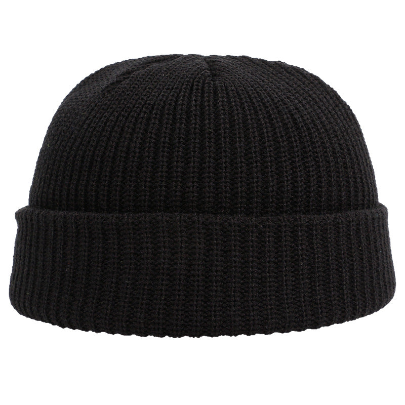 A black ribbed knit beanie with folded cuff displayed against white background, showing close-up texture of classic fisherman style