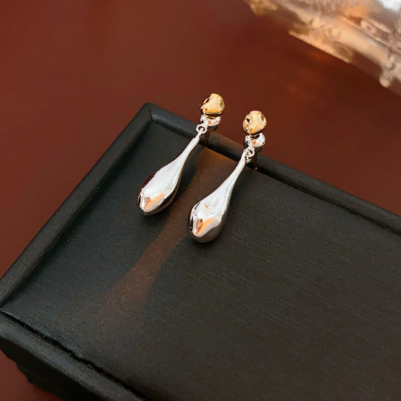Silver teardrop earrings with gold ball studs on textured background