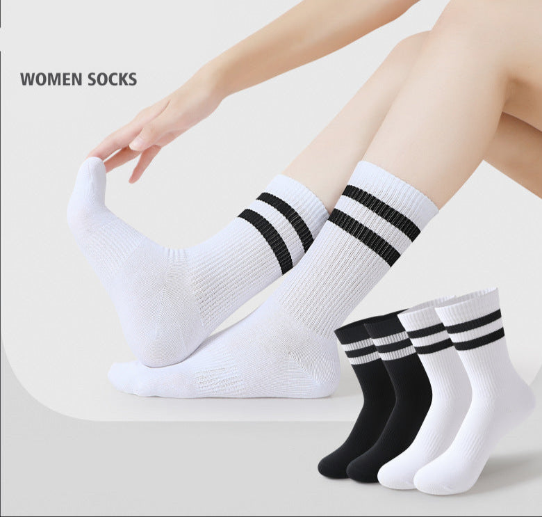A model is wearing white athletic crew socks with two black stripes, sitting on a white surface with legs slightly bent