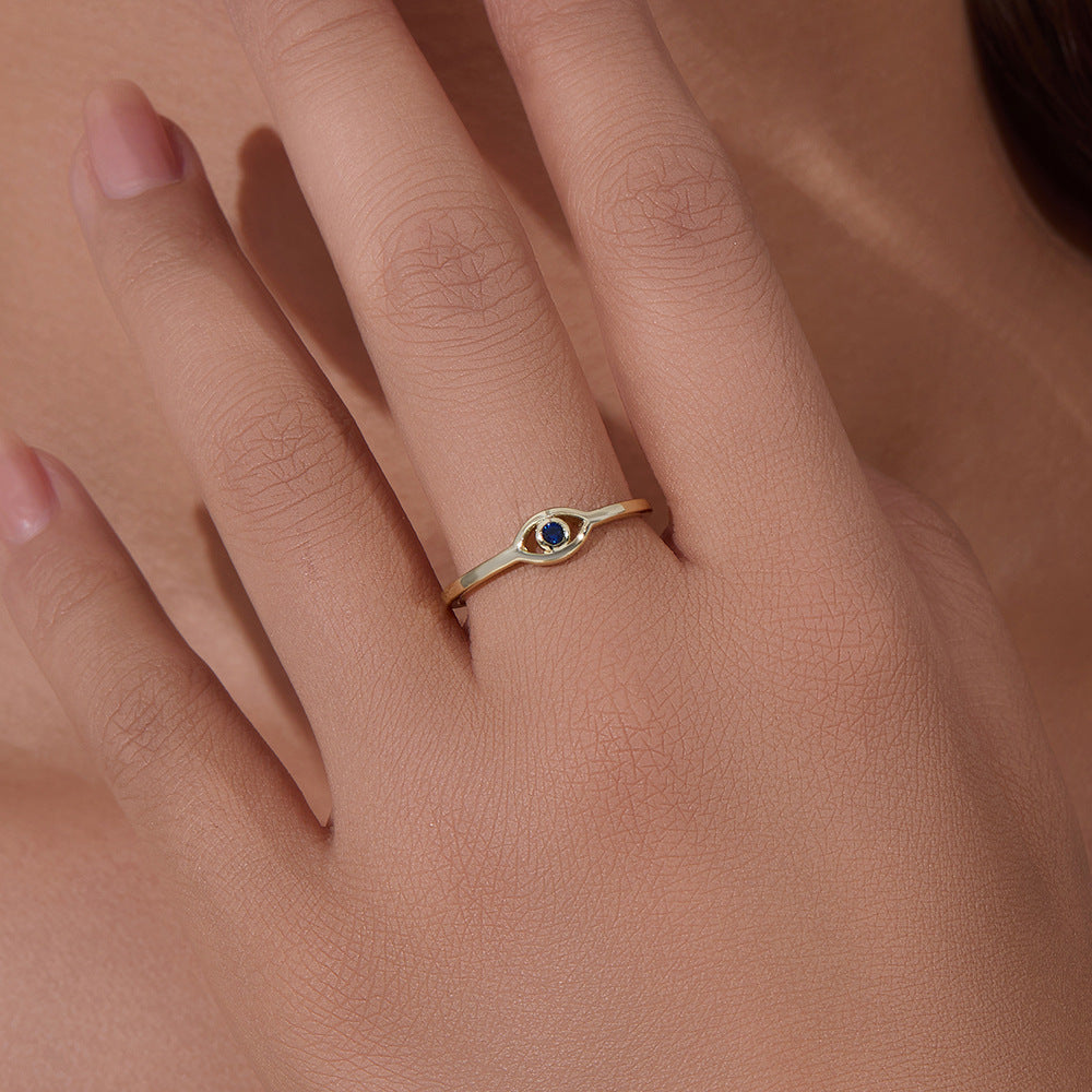 Close-up detail of gold eye ring with blue sapphire stone on a hand, showing natural skin texture