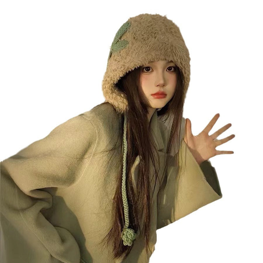 Cream-colored plush winter hat with mint green accents and braided tie, shown with oversized sage sweater
