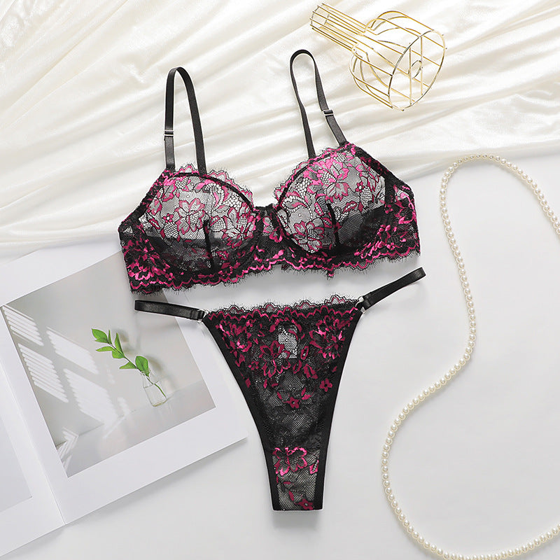 Black and pink lace lingerie set displayed on white fabric with pearl necklace and gold wire decor