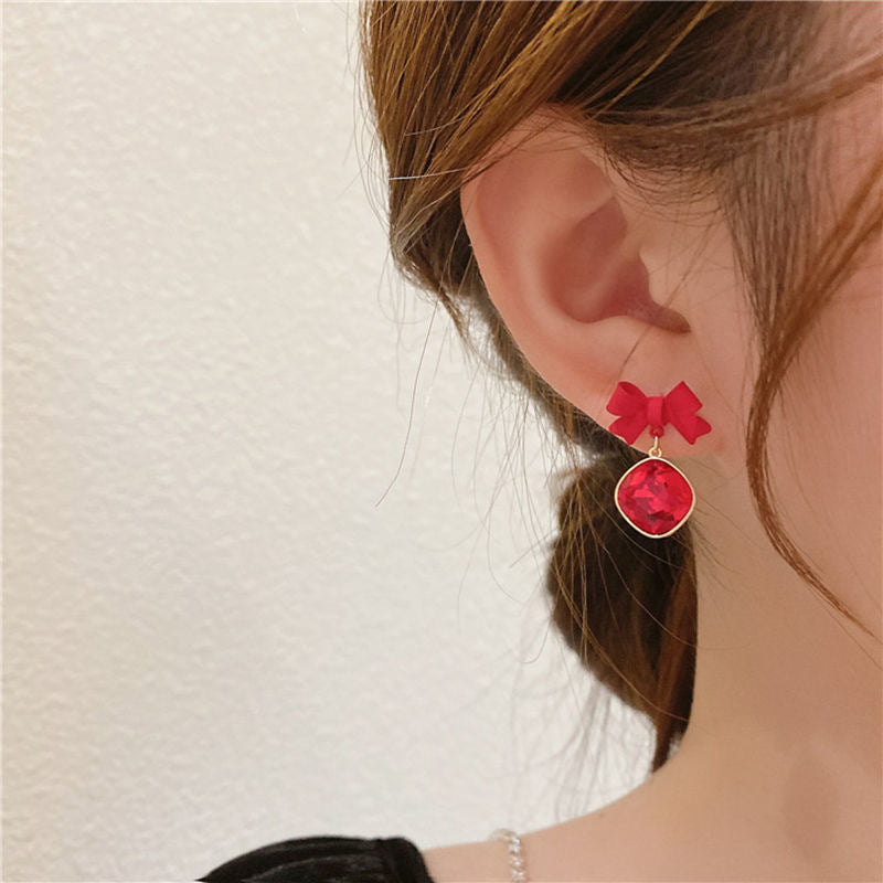 Close-up of an ear wearing a red bow earring with a matching red crystal pendant in gold setting