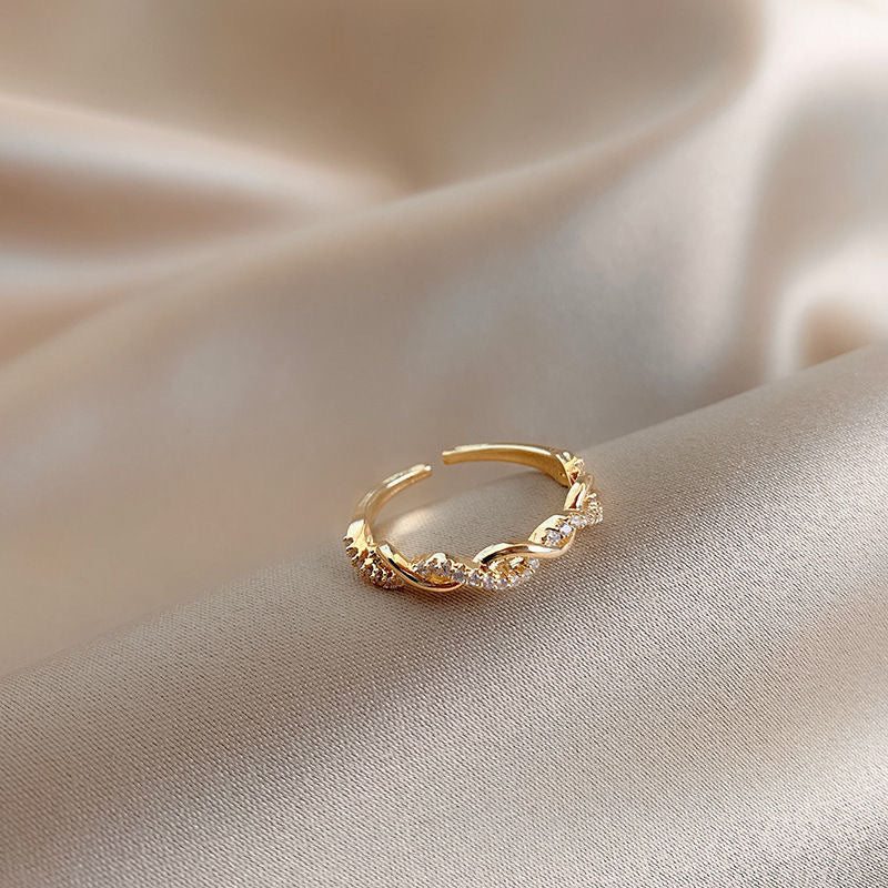 Gold twisted band ring with crystals photographed at angle on silk fabric