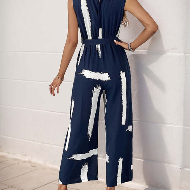 Back view of a women wearing navy sleeveless jumpsuit with a keyhole button closure, belted waist, and wide-leg pants.