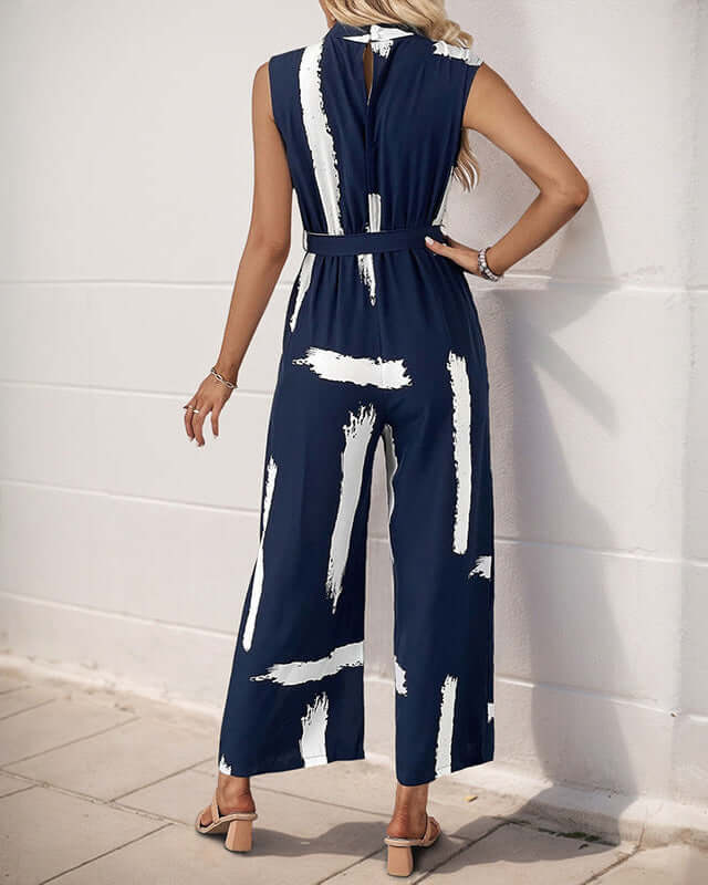 Back view of a women wearing navy sleeveless jumpsuit with a keyhole button closure, belted waist, and wide-leg pants.