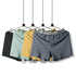 Four men's boxer shorts in black, mint, yellow and gray displayed on hangers showing front button fly design