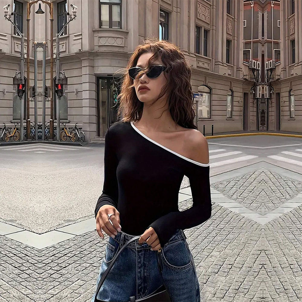 Black one-shoulder top with white trim, styled with dark sunglasses, curly hair, urban street background