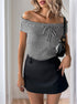Close-up of a woman wearing a gray off-shoulder ribbed top with a front tie, paired with a black mini skirt and black purse.