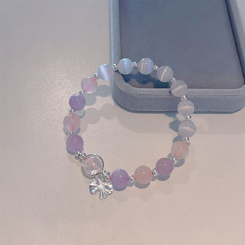 A stretch bracelet with alternating purple, pink and white opal beads featuring silver spacers and bow charm displayed on pale background