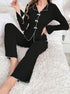 Close-up of black ribbed pajama top with white bow accents and trimmed collar, shown on plush white bedding