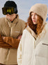 Models wearing NEIGTR STUDIO outerwear - man in tan jacket with black beanie and woman in cream jacket with knit beanie against snowy backdrop