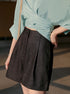 Close-up of black linen shorts with front pleats, paired with mint green top and beige shoulder strap accessory
