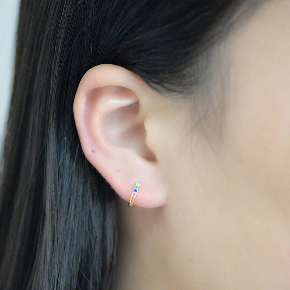 A woman wearing gold rainbow gemstone huggie earring in her earlobe against dark hair background
