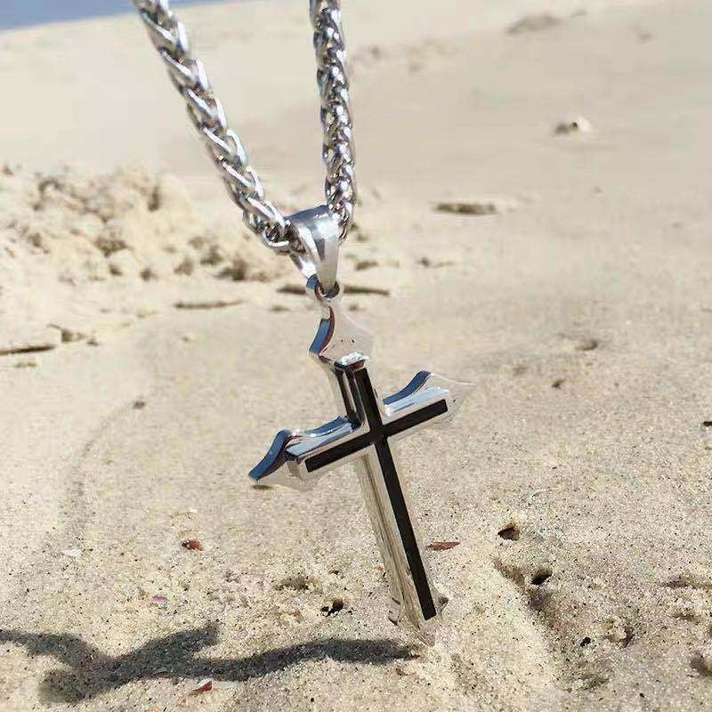 Silver cross pendant necklace with a black inlay, photographed on sand with a thick chain