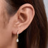 A woman wearing gold huggie hoop earring with teardrop crystal charm against brown hair background