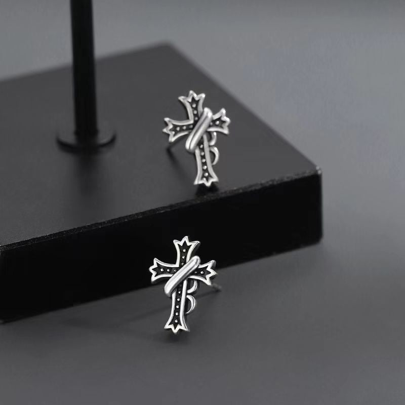 Cross stud earrings displayed on black geometric platform, showcasing detailed design