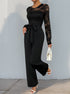 A side view of a woman in a black lace top jumpsuit with a cinched waist, holding a white handbag while stepping forward.