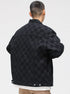 A model is showing the quilted lining of a black checkered jacket over white graphic tee and tan pants against white backdrop
