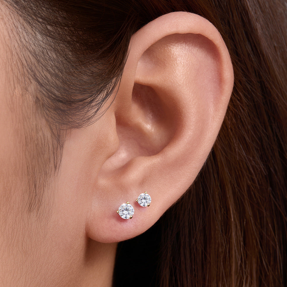 A woman wearing delicate diamond stud earrings in gold three-prong settings against brown hair background