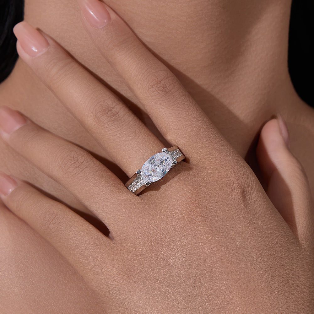 A woman's hand modeling silver oval diamond engagement ring with pave accents against neutral skin tone